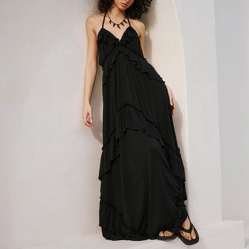 Black ruffled halter maxi dress leaning against a white wall.