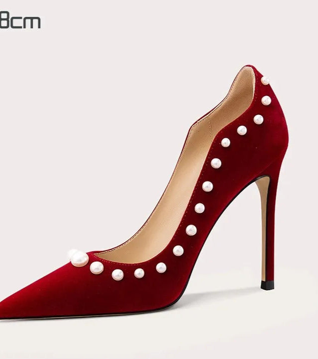 Red high-heeled shoe with pearl embellishments on a light gray background