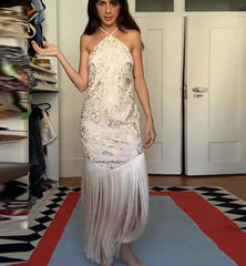 Woman in a white lace dress standing in a room with a mirror and door.