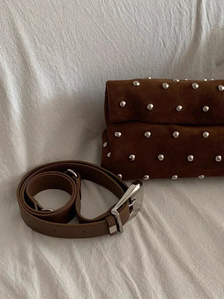 Brown leather belt and studded brown clutch on a white surface