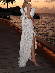 Woman in a white lace dress standing on a wooden pier by the ocean at sunset.