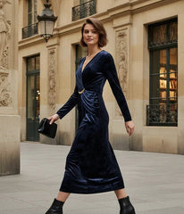 Woman in a navy velvet dress standing in an elegant courtyard.
