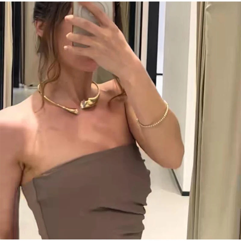 Woman wearing a strapless brown dress and gold jewelry in a mirror selfie.