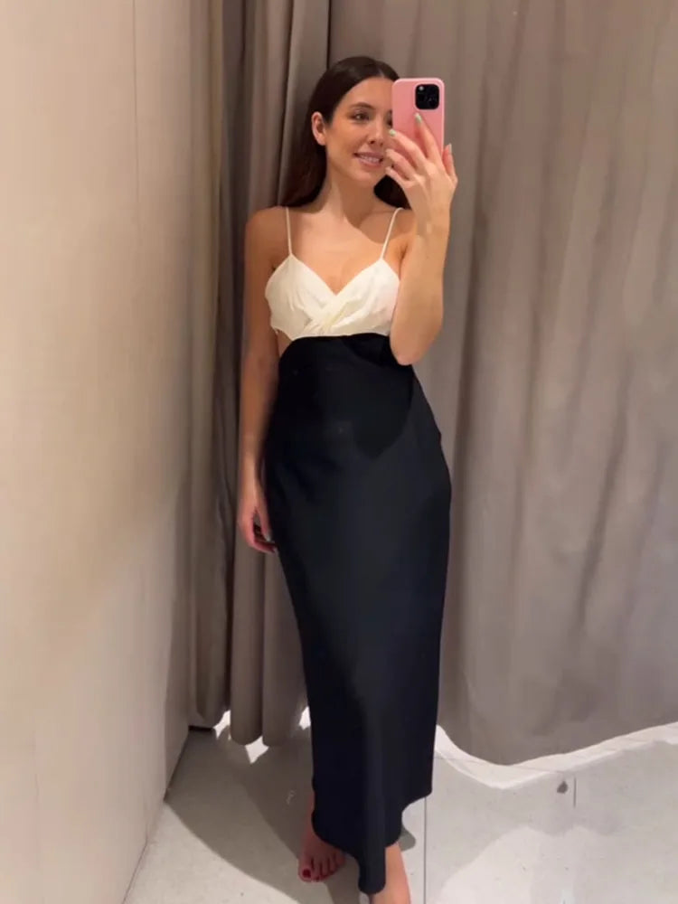 Woman taking a mirror selfie wearing a white top and black skirt against a plain background