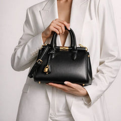 Structured lock top handle bag held by a person in a white blazer.