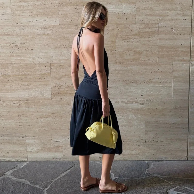 Woman in a black dress holding a yellow bag against a stone wall.