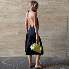 Woman in a black dress holding a yellow bag against a stone wall.