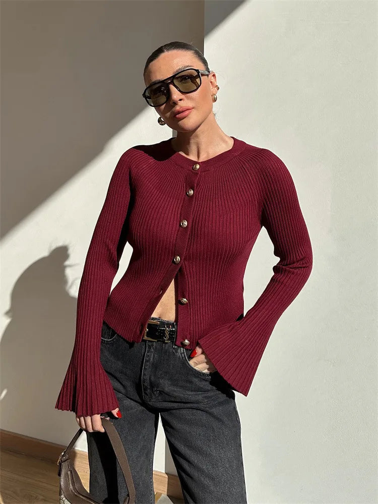 Woman wearing a red ribbed sweater and sunglasses against a neutral wall.