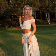 Woman in a white off-shoulder top and skirt standing in a grassy outdoor area.