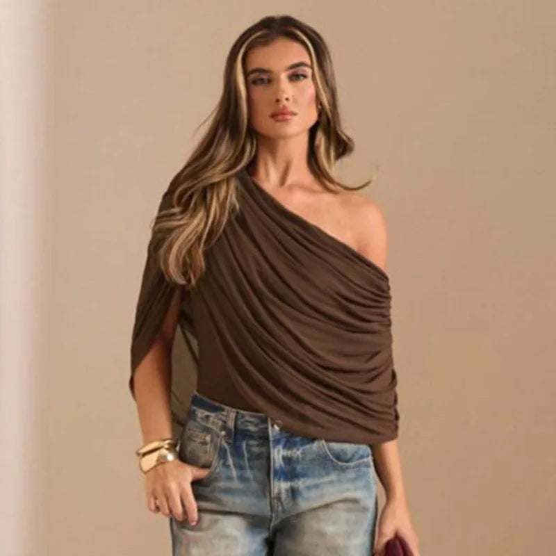 Woman wearing a brown one-shoulder top and blue jeans against a beige background