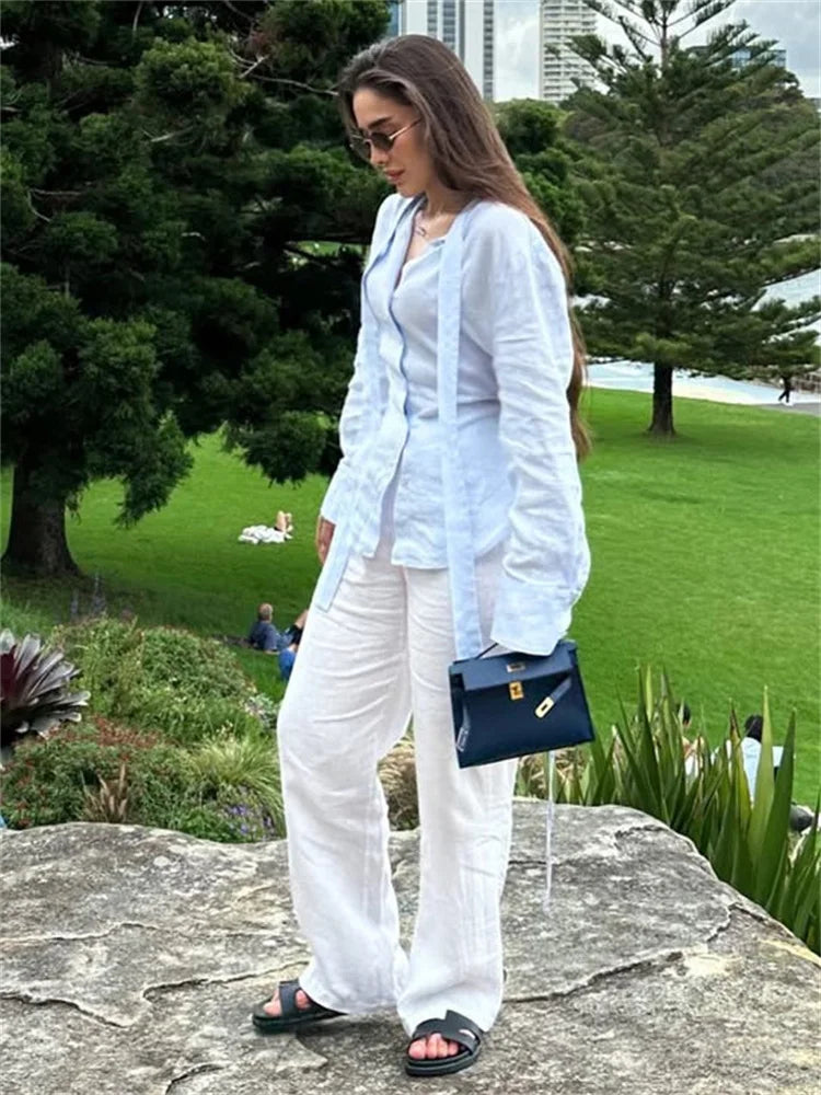Woman in white outfit standing on a rock with greenery and buildings in the background