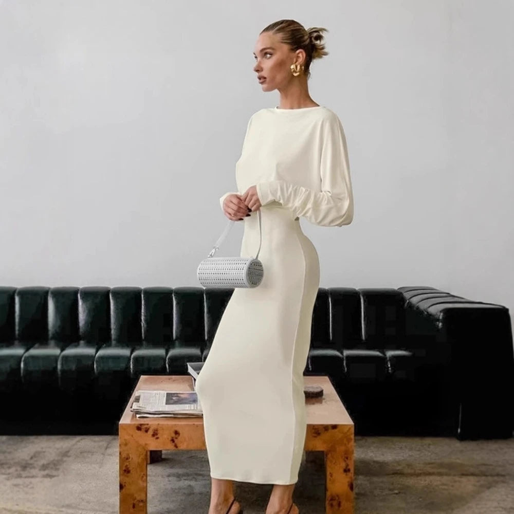 Woman in a white dress standing in a room with a black leather couch and wooden coffee table.