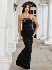 Woman wearing a black strapless dress with white embellishments in front of a classical building.