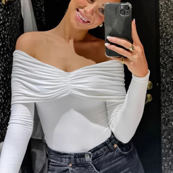 Woman taking a selfie wearing a white off-shoulder top and jeans.