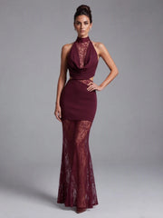 Model wearing a halter neck lace maxi dress with a fitted bodice and sheer overlay against a studio backdrop.