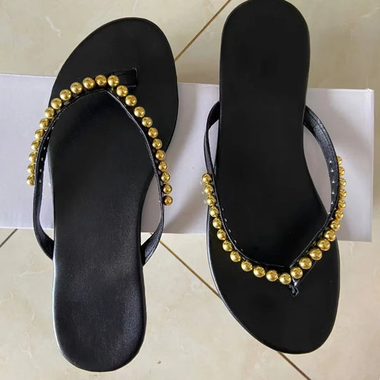 Pair of black flat embellished flip flops on a white surface.