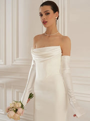 Woman in a white strapless gown holding flowers against a white wall.
