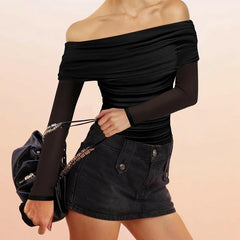 Person wearing a black off-shoulder top and black denim skirt holding a black handbag on a beige background