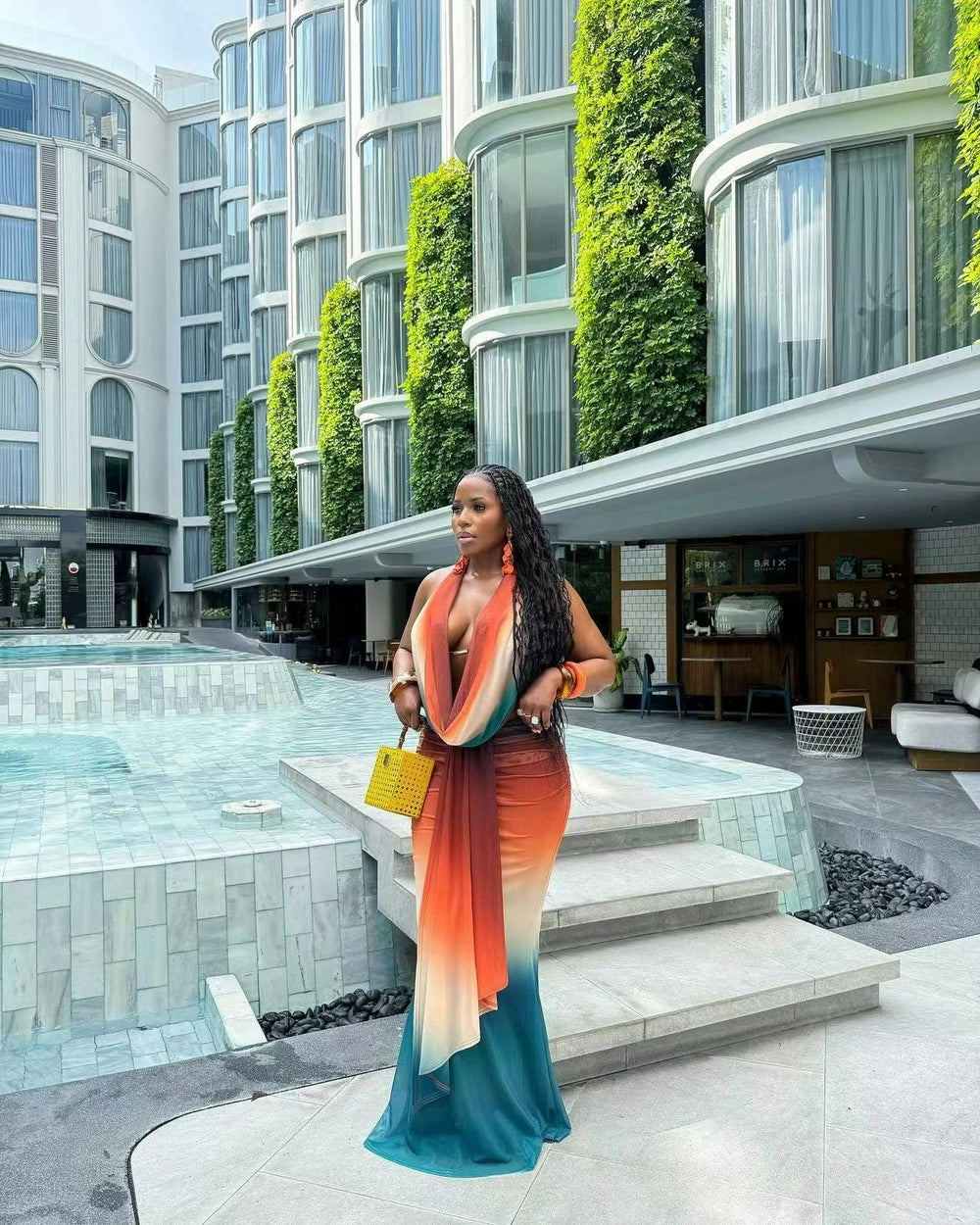 Woman in a colorful dress standing by a pool with modern building architecture in the background