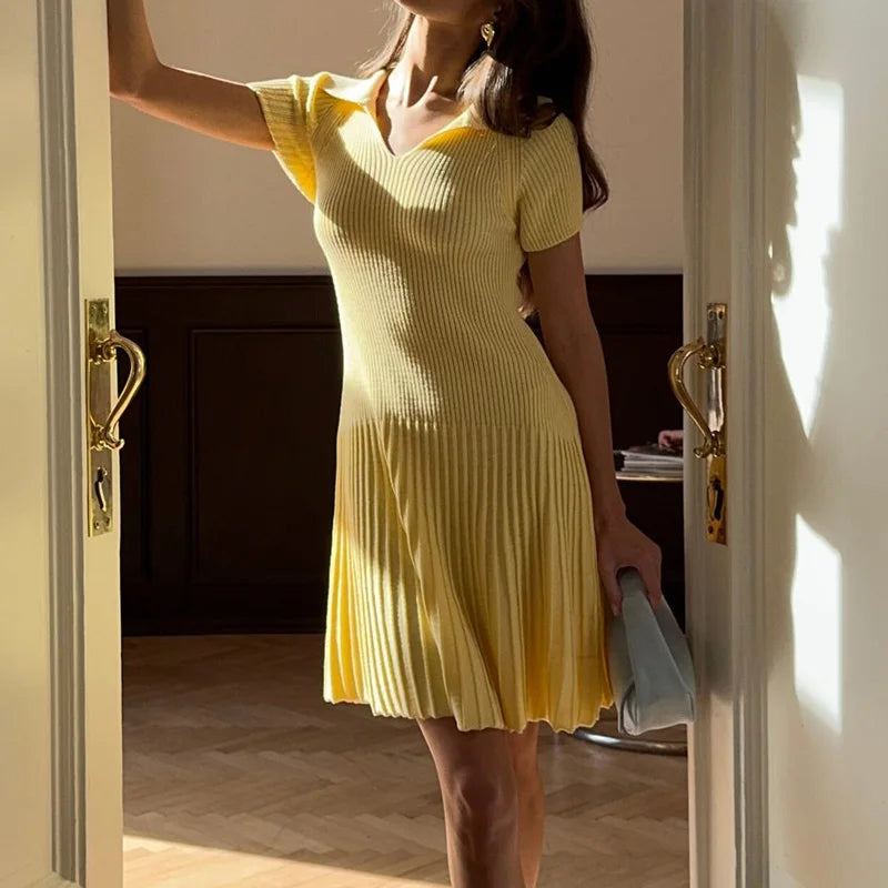 Woman in a yellow dress standing in a doorway holding a clutch.