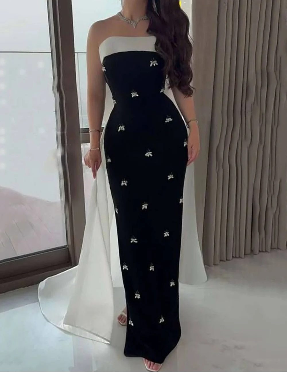 Woman wearing a strapless black and white dress with floral patterns indoors.