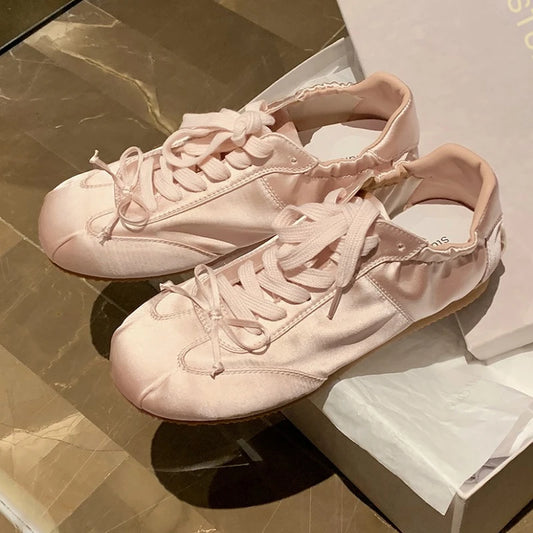 Pink satin ballet sneakers with round toe and lace-up closure.
