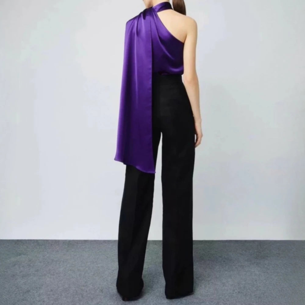 Person wearing a purple one-shoulder top and black pants against a plain background