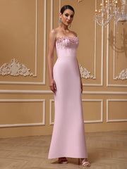 Woman wearing a pink strapless gown in an elegant room with decorative wall molding and a chandelier.