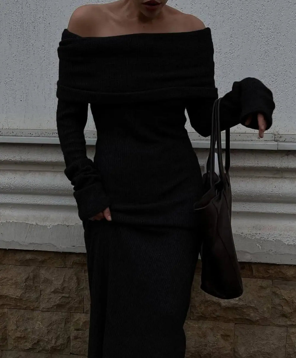 Person wearing a black off-shoulder dress holding a black handbag against a neutral background