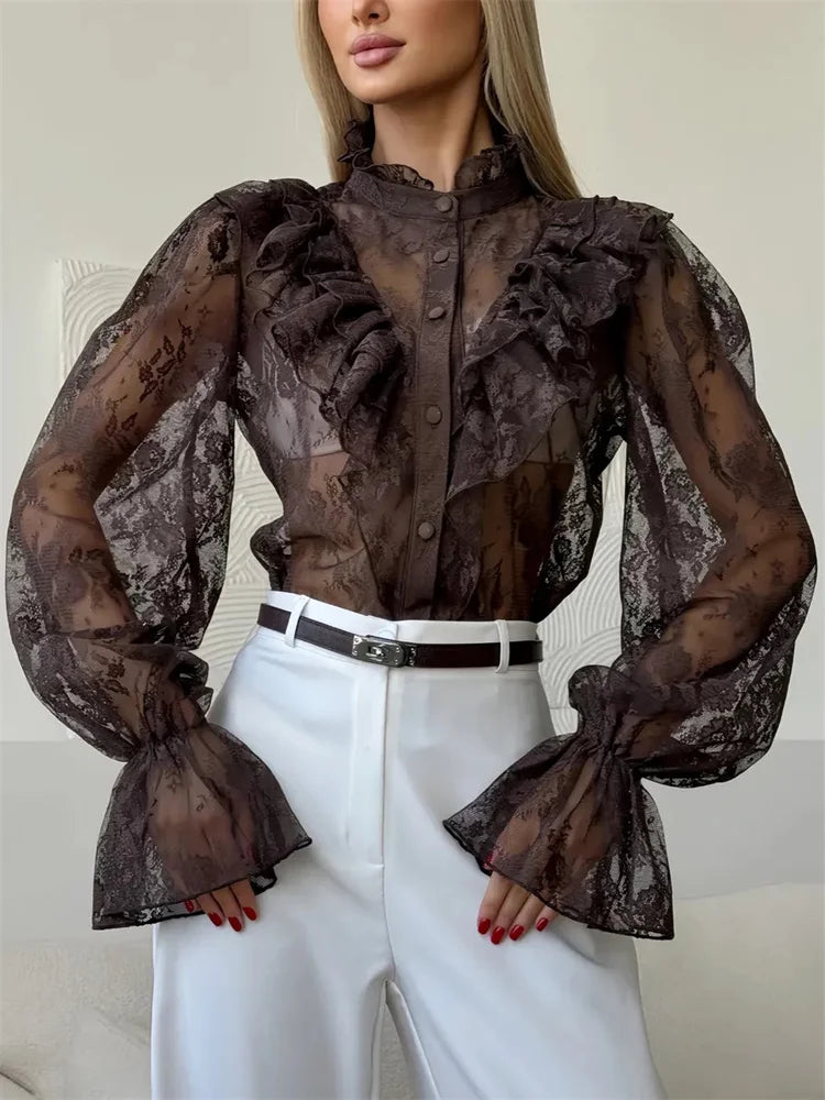 Woman wearing a sheer black lace blouse with white pants against a neutral background