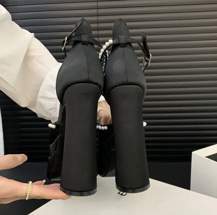 Black high-heeled shoes with pearl details on a white surface.