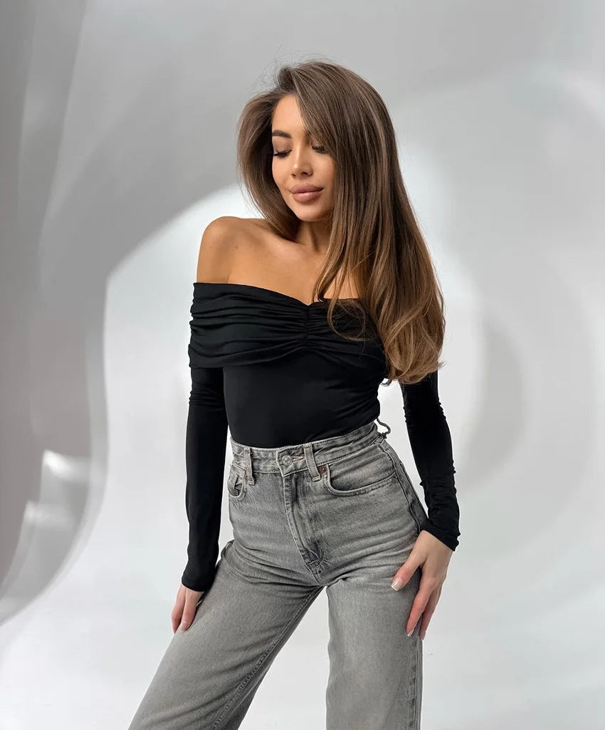 Woman wearing a black off-shoulder top and gray jeans against a light gray background