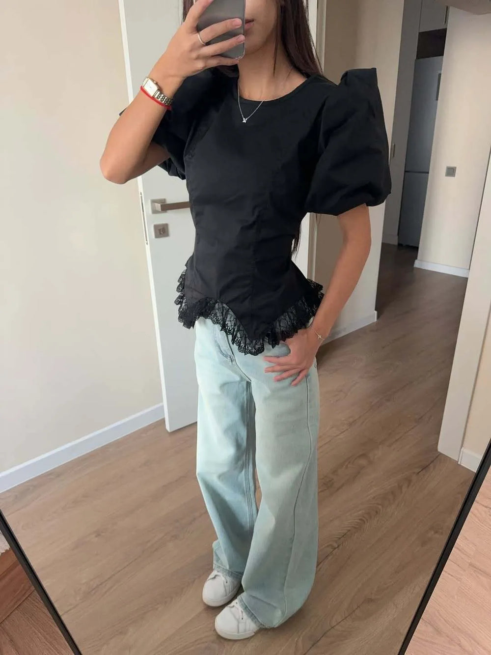 Person wearing a black top with puffed sleeves and light blue jeans, standing in a room.