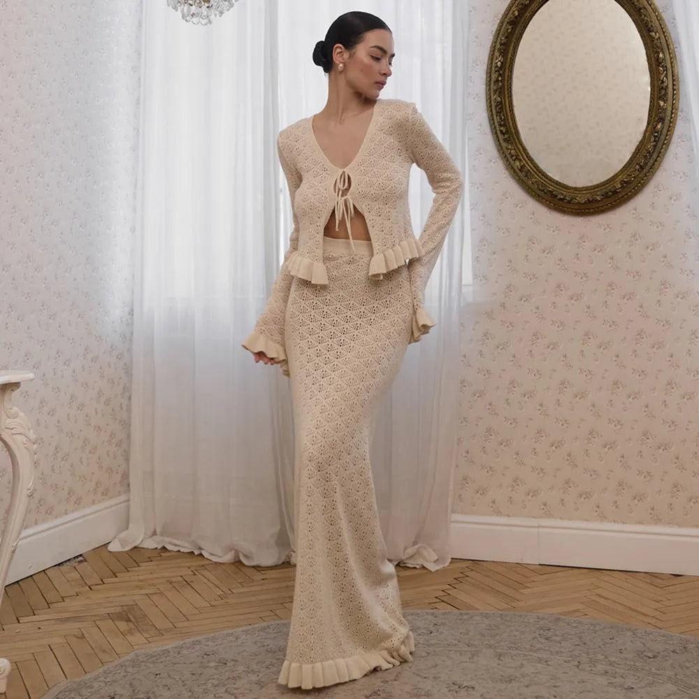 Woman in a beige knitted outfit standing in a room with decorative walls and a mirror.