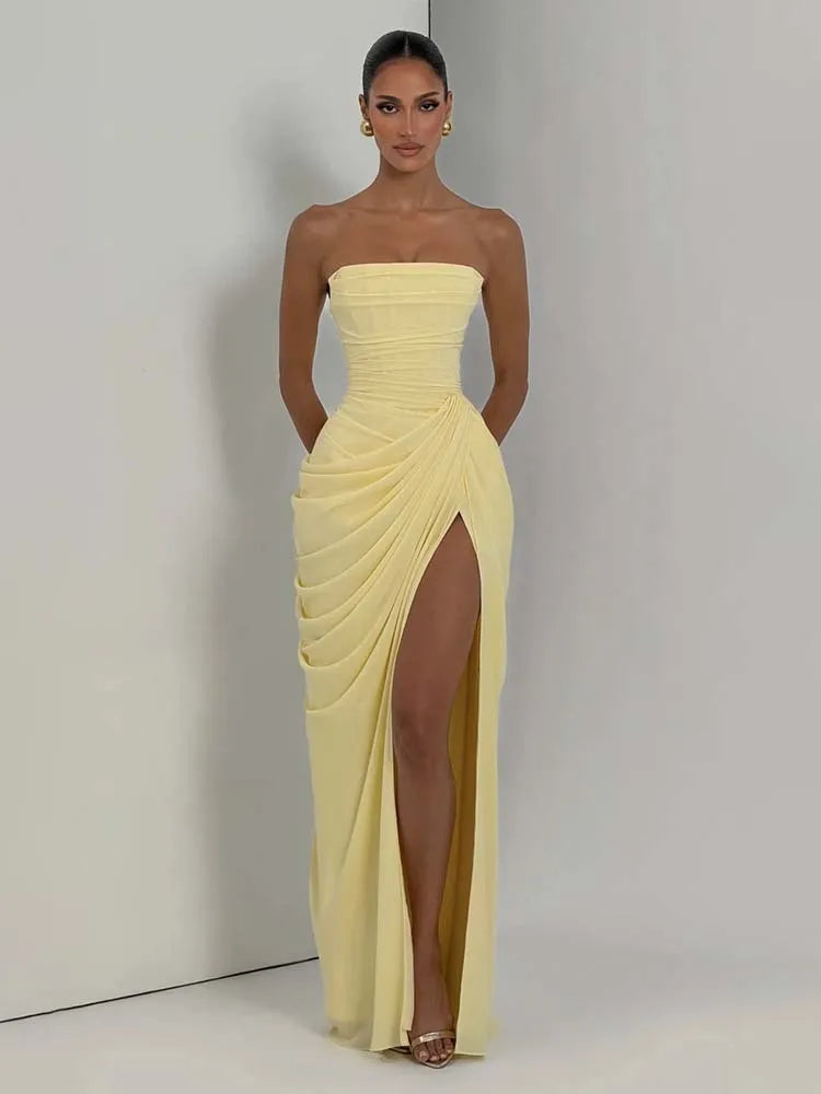 Woman wearing a strapless yellow evening gown with a high slit on a plain background