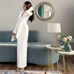 Woman in a white outfit standing in a modern living room with a blue sofa and decorative elements.