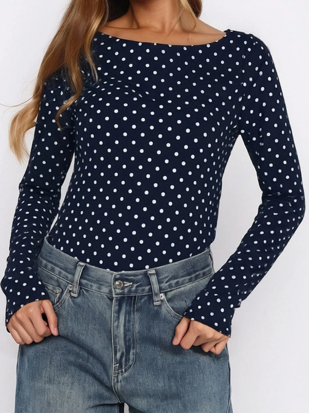 Navy blue long-sleeve top with white polka dots worn by a person on a plain background