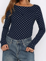 Navy blue long-sleeve top with white polka dots worn by a person on a plain background