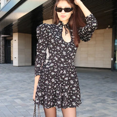 Woman wearing a black floral dress and sunglasses outdoors.