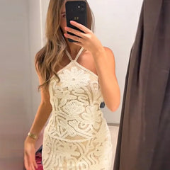 Woman wearing a beige lace dress taking a mirror selfie.