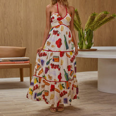 Woman wearing a colorful dress with food print in a room with a wooden floor and a vase of flowers.