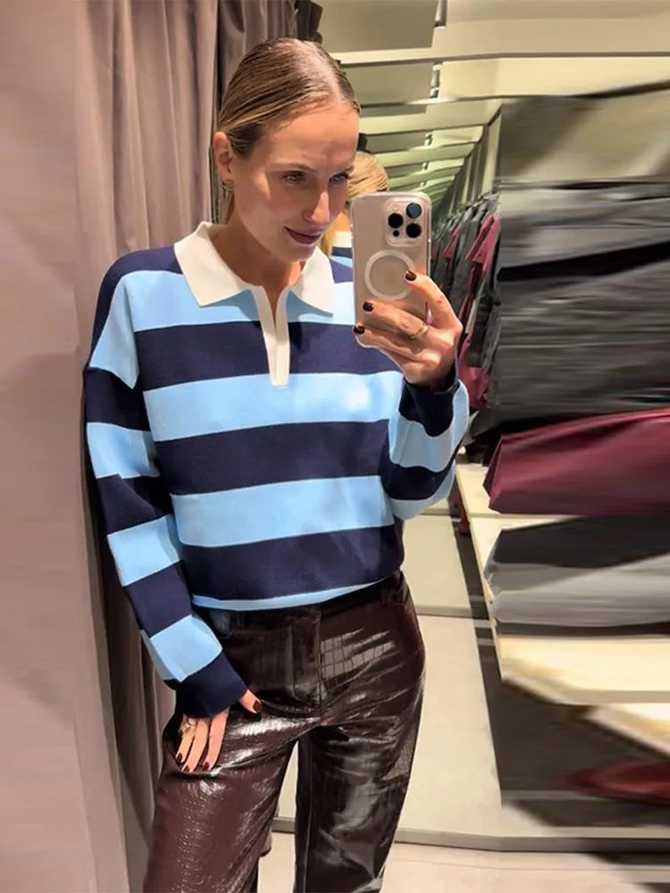 Person wearing a striped sweater and leather pants taking a mirror selfie.
