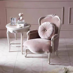 Pink armchair with decorative pillow in a room with a small round table.
