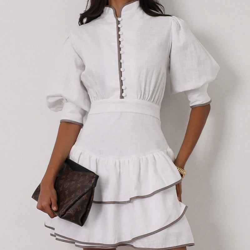 White dress with long sleeves and a brown clutch on a plain background
