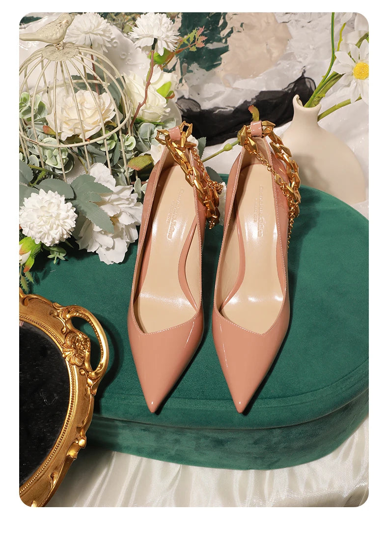 Pair of pink high heels with gold chains on a decorative surface with flowers and a mirror.