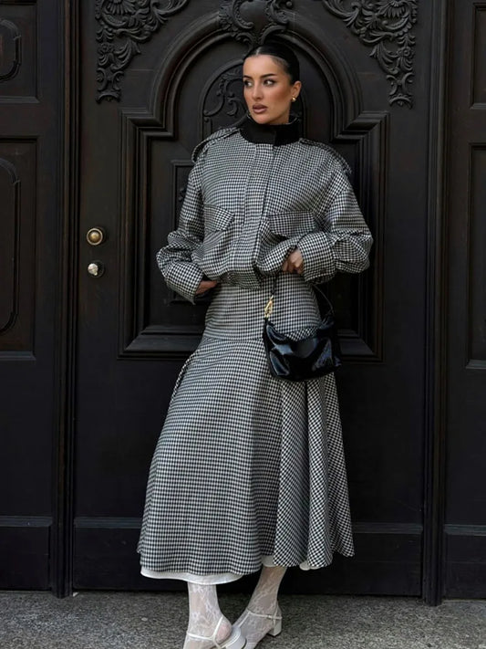 Woman in a checkered outfit standing in front of a dark door.