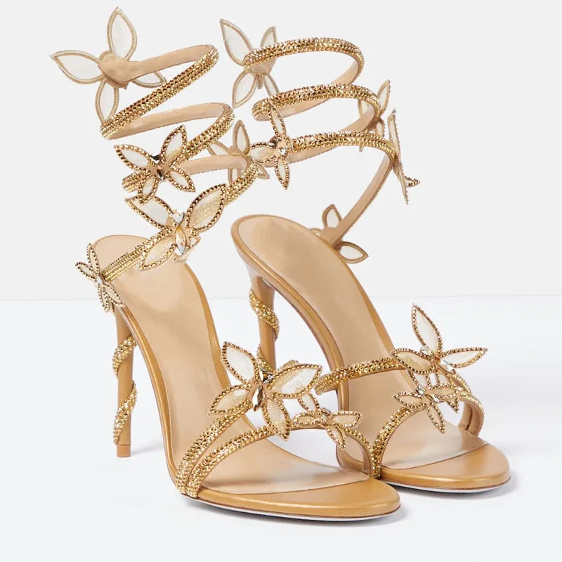 Gold high-heeled sandals with decorative straps on a light gray background