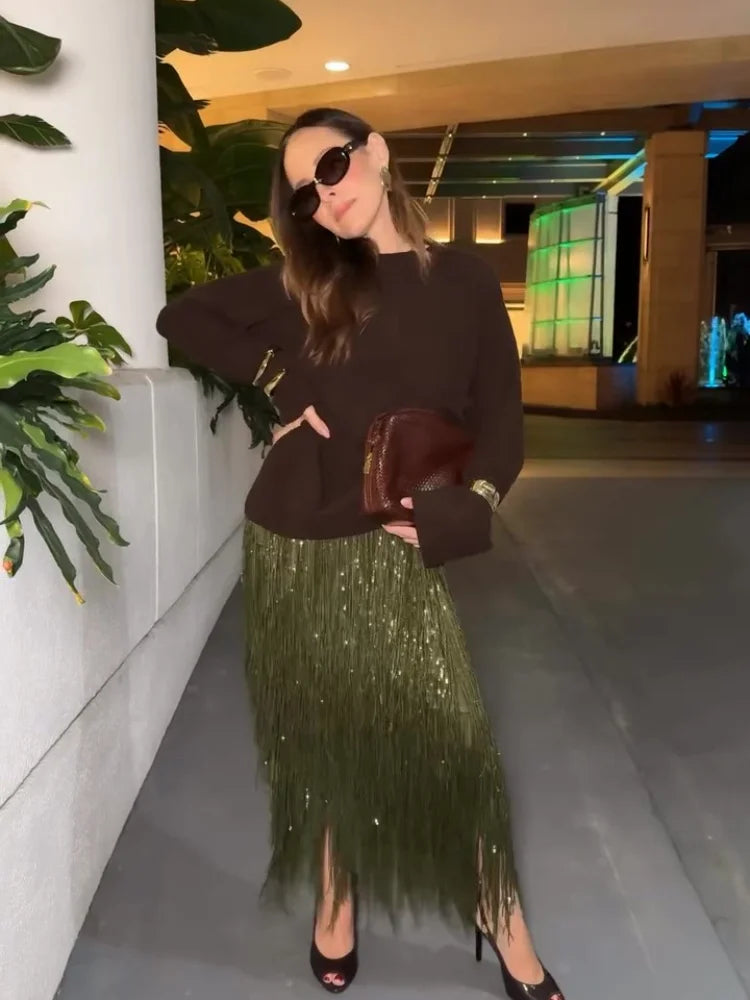 Woman in a dark sweater and green sequin skirt standing indoors.
