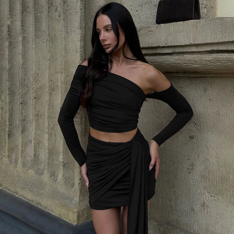 Woman wearing a black off-shoulder dress standing against a textured wall.