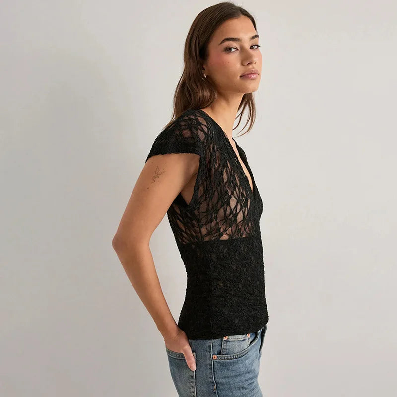 Woman wearing a black lace top and jeans on a plain background